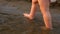 Small baby in diaper takes its first steps walking along river bank. Legs. Close-up. Slow motion