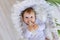 A small baby girl lies in a beautiful cradle in a white bodysuit at home and holds a bottle of milk in her hands