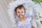 A small baby girl lies in a beautiful cradle in a white bodysuit at home and holds a bottle of milk in her hands