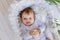 A small baby girl lies in a beautiful cradle in a white bodysuit at home and holds a bottle of milk in her hands