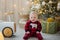 Small baby sit under chrismas tree with light and presents