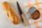 Small baguette, knife, opened jar with pollock roe on napkin on wooden table. Top view