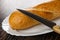 Small baguette, knife in white dish on wooden table