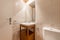Small bathroom with porcelain sink on wooden cabinet with shelf and drawers, cream tile, and frameless rectangular mirror