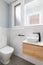 Small bathroom with toilet and designer sink on small vanity with black faucet. Walls of room are made of white natural