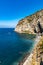 Small beach full of colorful sunbeds and umbrellas next to high cliff