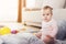 A small beautiful baby sits on the floor and plays with bright, flowery toys.