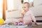 A small beautiful baby sits on the floor and plays with bright, flowery toys.