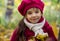 A small beautiful girl with big eyes smiling in warm autumn, wearing a pink beret and a coat with dry leaves in hands.