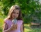 A small, beautiful white girl in a dress, in the summer, drinks cooling lemonade outdoors. Portrait of a smiling girl