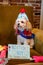 Small beige Havanese puppy dog sitting on a chair wearing a homemade birthday hat and bandana with a birthday sign.