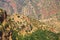 Small  berber village with clay houses on hill top against impressive red mountain face dotted with green plants