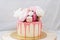 Small birthday cake with melted pink chocolate, fresh peonies, macaroons and meringues on white background.