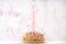 Small birthday cake with one candle over soft pink background with copy space