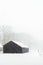 Small black wooden barn in snowy countryside during snowfall.