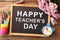 Small blackboard with text Happy Teacher`s Day, stationery and flowers on wooden table, top view