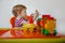 A small blond boy at home sitting at an orange children's table playing a colorful plastic construction kit