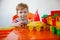 A small blond boy at home sitting at an orange children's table playing a colorful plastic construction kit