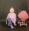 Small blond girl and dolls pram on black background. Little girl sits on black background.