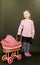 Small blond girl and dolls pram on black background. Little girl stands on black background.