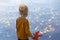 Small blond girl with red maple leaf in her hand watching autumn yellow leaves floating in the lake