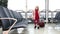 Small blonde girl in winter coat with suitcase sitting on a black chair in a waiting hall in the airport.