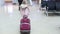Small blonde girl in winter coat with suitcase walking across waiting hall in the airport.