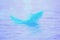 A small blue feather floats on water waves.