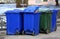 Small blue and green plastic dumpsters stand in the courtyard of a residential building
