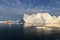 A small boat among icebergs. Sailboat cruising among floating icebergs in Disko Bay glacier during midnight sun Greenland