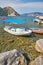 small boats moored in Aegean sea blue lagoon with mountainous islands around, beach at background and turkish flag at top of hill