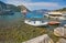 small boats moored in Aegean sea blue lagoon with mountainous islands around, beach at background and turkish flag at top of hill