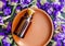 Small bottle with essential oil on the small ceramic plate. Dark wooden background with dry purple flowers. Aromatherapy and spa