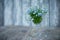 A small bouquet of forget-me-nots in a crystal glass on a blurred background of boards painted with blue paint and a few flowers o