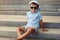 Small boy in blue sunglasses sitting on concrete stairs outdoors