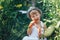 small boy farmer kid sitting in line of tomatoes plants, wearing white casual overalls suit and grey hat, eating carrot, harvest