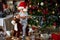 Small boy in Santa hat riding wooden rocking horse in front of christmas tree
