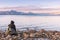 Small boy sits on rock by Okanagan Lake with sunset view of snow covered mountains