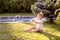 A small boy is sitting on the grass near a blue spruce. The boy drinks milk.