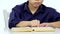 Small boy sitting at a table and reads interesting book slowly. White background. Close up