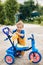A small boy stands next to a child's tricycle. First bike, new skills