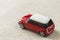 Small bright red metal simple child toy car with dark windows on light beige canvas cloth copy space background