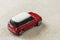 Small bright red metal simple child toy car with dark windows on light beige canvas cloth copy space background