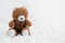 Small brown bear doll with red and green plaid pattern bow placed on fluffy carpet. White background