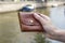 Small brown stitched wallet in a female hand on a blurred background of a river with boats