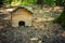 Small brown wooden hedgehog house on the lush green forest ground