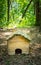 Small brown wooden hedgehog house on the lush green forest ground