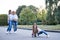 Small brunette girl,wearing blue jeans and white shirt holding white and brown dog in city park in summer with two women at the