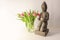 Small buddha statue from ceramic with a lit candle and a bouquet of pink tulips on a light background, copy space