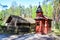 A small burgundy wooden chapel and a gray village house with a thatched roof and hedge